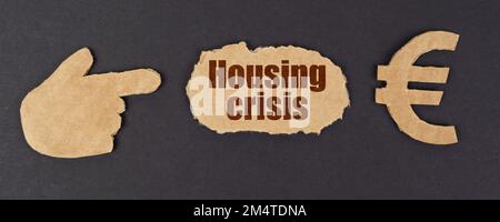 Economy and finance concept. On a black surface, a figure of a hand, a euro symbol and a torn cardboard with the inscription - Housing Crisis Stock Photo