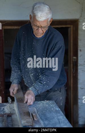 vertical photo of a carpenter working on a circular saw in his workshop. clothes dirty from sawdust. Stock Photo