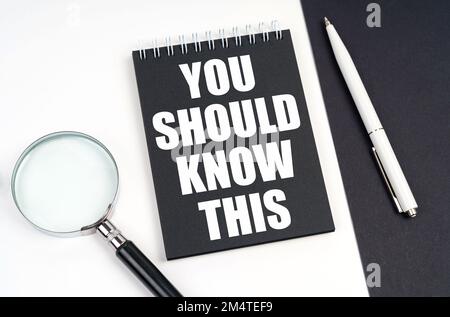 Business and economy concept. On a black and white surface lies a magnifying glass, a pen and a notepad with the inscription - You Should Know This Stock Photo