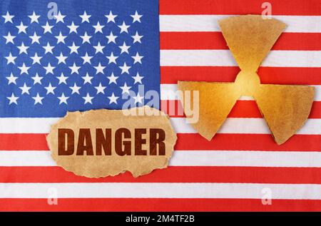 Industry and radiation concept. On the flag of the United States, there is a symbol of radioactivity and a torn cardboard with the inscription - Dange Stock Photo