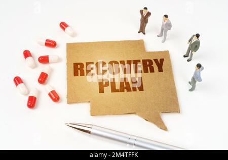 Medical concept. On a white surface are pills, a pen, miniature figurines of people, a sign with the inscription - RECOVERY PLAN Stock Photo