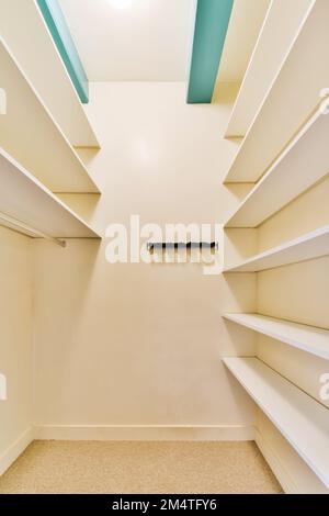 a walk - in closet with white shelvings and shelves on the wall, there is an open door Stock Photo