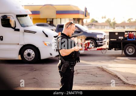 White male caucasian police officer cop standing on street in black uniform, gun on hip, radio walkie talkie talking to dispatch during the day gettin Stock Photo