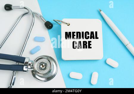 Medical concept. On a white and blue surface are pills, a stethoscope, a pen and a notepad with the inscription - MEDICAL CARE Stock Photo