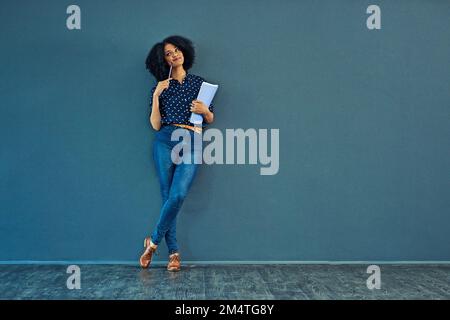 Dreams were meant to be followed. Studio shot of a young woman holding a book and looking thoughtful against a gray background. Stock Photo