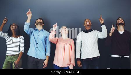 Woah Whats that. Studio shot of a diverse group of people pointing upwards against a gray background. Stock Photo