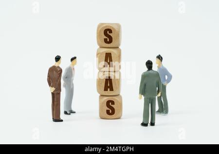 Technology and business concept. On a white background, figures of businessmen look at wooden cubes with the inscription - SAAS Stock Photo