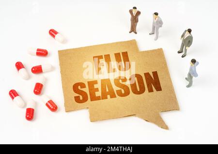 Medical concept. On a white surface are pills, a pen, miniature figurines of people, a sign with the inscription - FLU SEASON Stock Photo