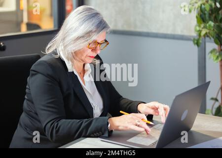 senior middle aged business woman using laptop working on computer sitting at desk. business woman working on computer Stock Photo