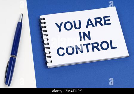 Business and finance concept. On a blue-white surface lies a pen and a notebook with the inscription - You Are In Control Stock Photo