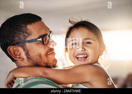 Such a happy girl. Portrait of a cheerful little girl being held in her fathers arms inside at home during the day. Stock Photo