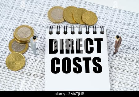 Business and finance concept. On financial reports there are figurines of people, coins and a notepad with the inscription - DIRECT COSTS Stock Photo