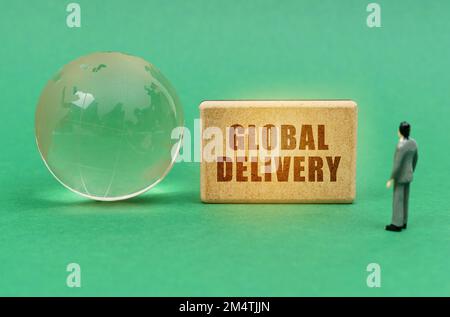 Business and transport concept. On the green surface is a globe and a figurine of a man who looks at a sign with the inscription - Global delivery Stock Photo