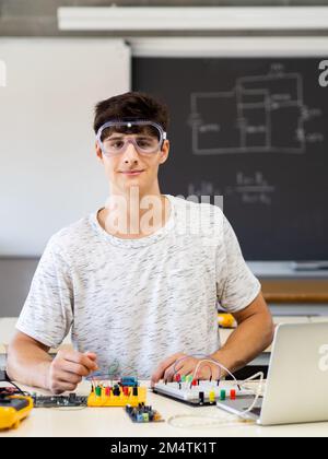 Young male technology student looking at camera with protective glasses in electronics class Stock Photo