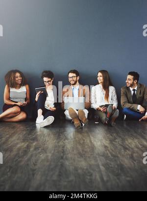 Connecting with the teammates. Studio shot of a group of businesspeople using wireless technology and talking on the floor against a gray background. Stock Photo