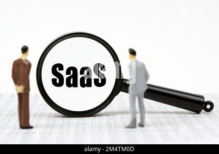 Business and finance concept. On the financial reports there are miniature figures of businessmen and a magnifying glass with the inscription - SaaS Stock Photo