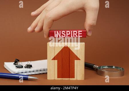 Business concept. On a brown surface are office items, wooden blocks, in the hand is a red block with the inscription - Inspire Stock Photo