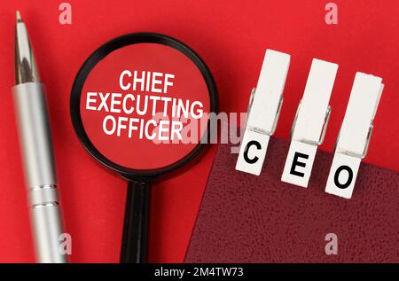 Business concept. On the red surface lies a pen, a notebook with clothespins - CEO, and a magnifying glass with the inscription - Chief Executting Off Stock Photo