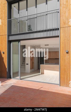 Glass doors in black metal frame open onto house with spacious kitchen with light wooden furniture and staircase to second floor. Doors connect the Stock Photo