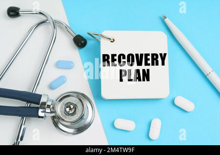 Medical concept. On a white and blue surface are pills, a stethoscope, a pen and a notepad with the inscription - RECOVERY PLAN Stock Photo
