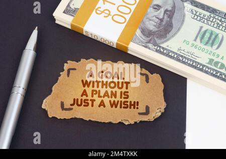 Business concept. On the table are dollars, a pen and a cardboard sign with the inscription - a goal without a plan is just a wish Stock Photo