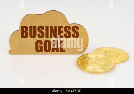 Business and technology concept. Bitcoins lie on a white surface and there is a sign - a cloud with the inscription - BUSINESS GOAL Stock Photo