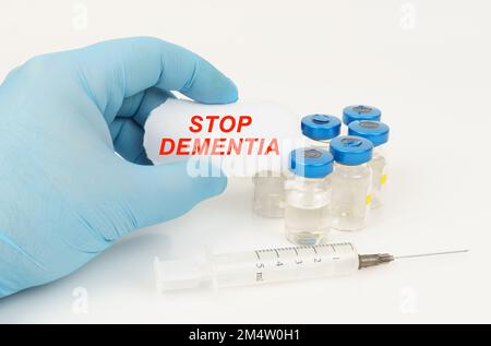 Medical concept. In the man's hand is a piece of paper with the inscription - STOP DEMENTIA, next to it lies a syringe and injection jars. Stock Photo