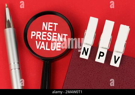 Business concept. On the red surface lies a pen, a notebook with clothespins - NPV, and a magnifying glass with the inscription - Net Present Value Stock Photo