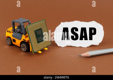 Technological concept. On a brown surface, a forklift is transporting a processor, next to it is paper with the inscription - ASAP Stock Photo