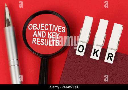 Business concept. On the red surface lies a pen, a notebook with clothespins - OKR, and a magnifying glass with the inscription - Objectives and Key R Stock Photo