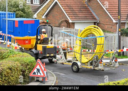 Gas main contractor worker driving dumper truck towing trailer loaded with large coil yellow plastic tube to insert inside old steel pipe England UK Stock Photo