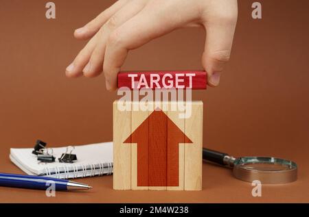 Business concept. On a brown surface are office items, wooden blocks, in the hand is a red block with the inscription - Target Stock Photo