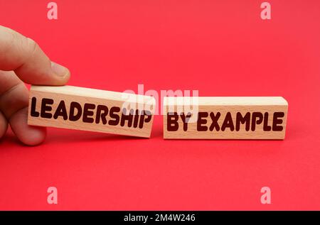 Business concept. On a red background, wooden blocks, one of them in hand. The blocks are written - LEADERSHIP BY EXAMPLE Stock Photo
