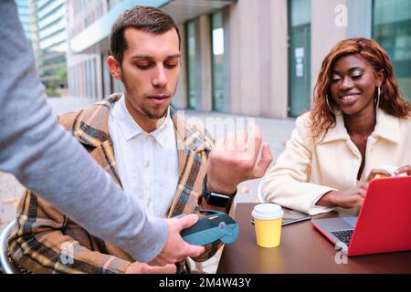 Man making contactless payment with smartwatch at a coffee shop. Stock Photo