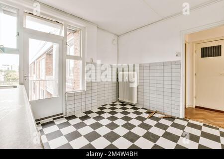 an empty room with black and white checkered tiles on the floor, in front of a large open window Stock Photo