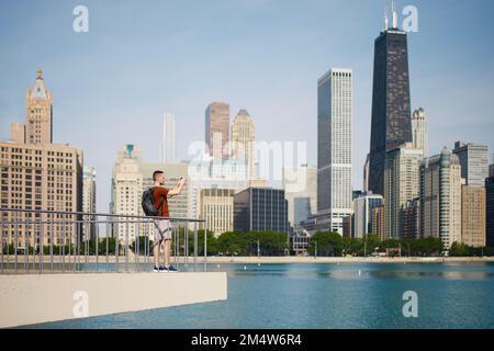 View of Chicago skyline with skyscrapers. Selective focus on young man while photographing cityscape with smart phone. Stock Photo