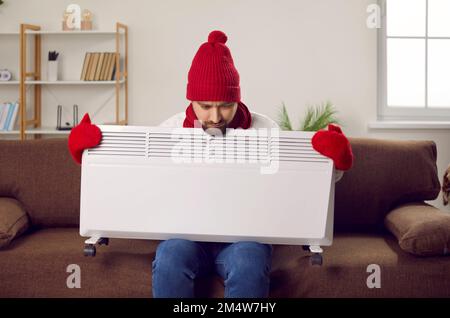 Man trying to warm up with an electric heater when it's very cold in the house in winter Stock Photo