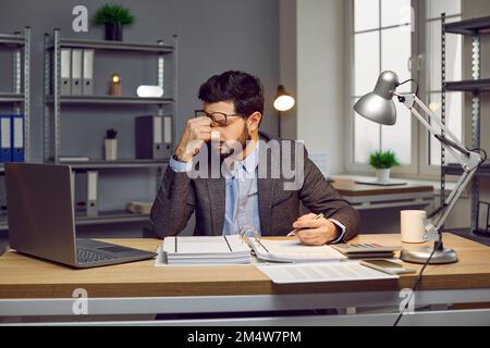 Overworked businessman taking off glasses feeling eyestrain sitting at desk Stock Photo