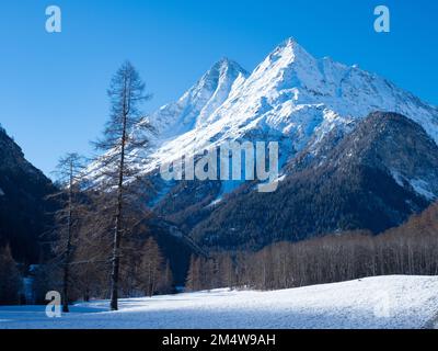 Val d'Herens, Switzerland - April 10th 2022: Winter wilderness in the Alps - a snowy field in front of forests and peaks Stock Photo