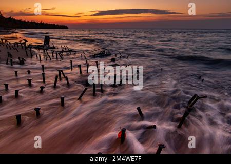 Lake Superior shipwreck timbers lie on the shores as waves ebb in and out among the wreckage, under a Great Lakes sunset on the Graveyard Coast USA Stock Photo