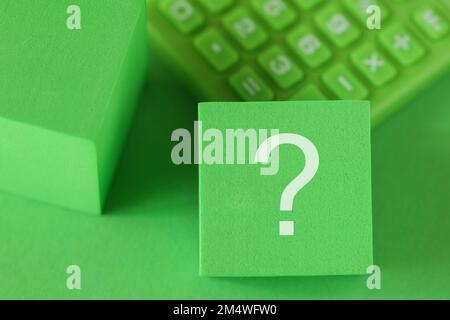 Question mark sign on block cube, green calculator, green background. ESG support concept Stock Photo