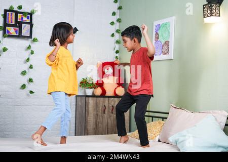 Happy smiling sibling kids dancing by jumping on bed at home - concept of playful childhood, bonding and relationship. Stock Photo