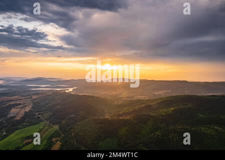 An aerial shot of forested mountains with the sun shining behind the clouds Stock Photo