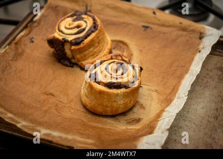 Freshly cooked, homemade cinnamon rolls out of the oven on a baking tray with brown paper. Stock Photo