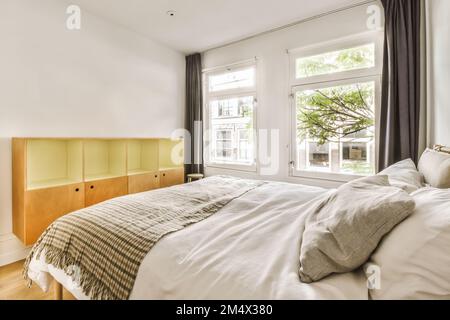 a bedroom with a bed, dresser and large window in the photo is taken to the right side of the room Stock Photo