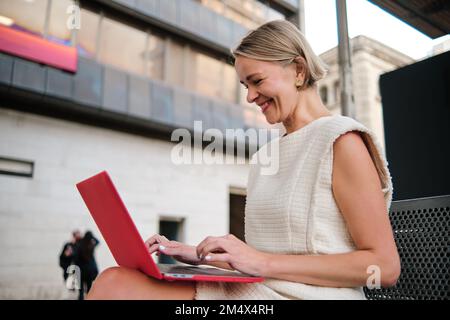 Businesswoman smiling while using a laptop sitting outdoors. Stock Photo