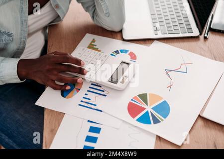 Businesswoman using calculator with diagrams on desk at home Stock Photo