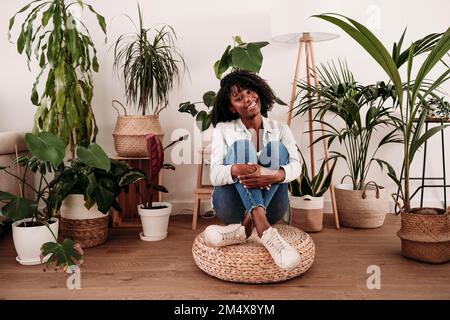 Smiling woman hugging knees sitting on hassock at home Stock Photo