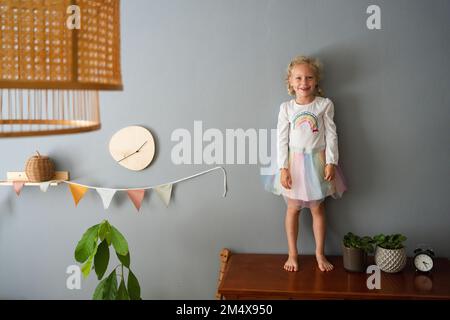 Smiling cute girl standing on table at home Stock Photo