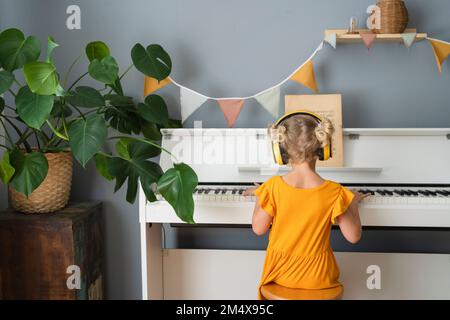 Girl listening music on headphones and playing piano at home Stock Photo